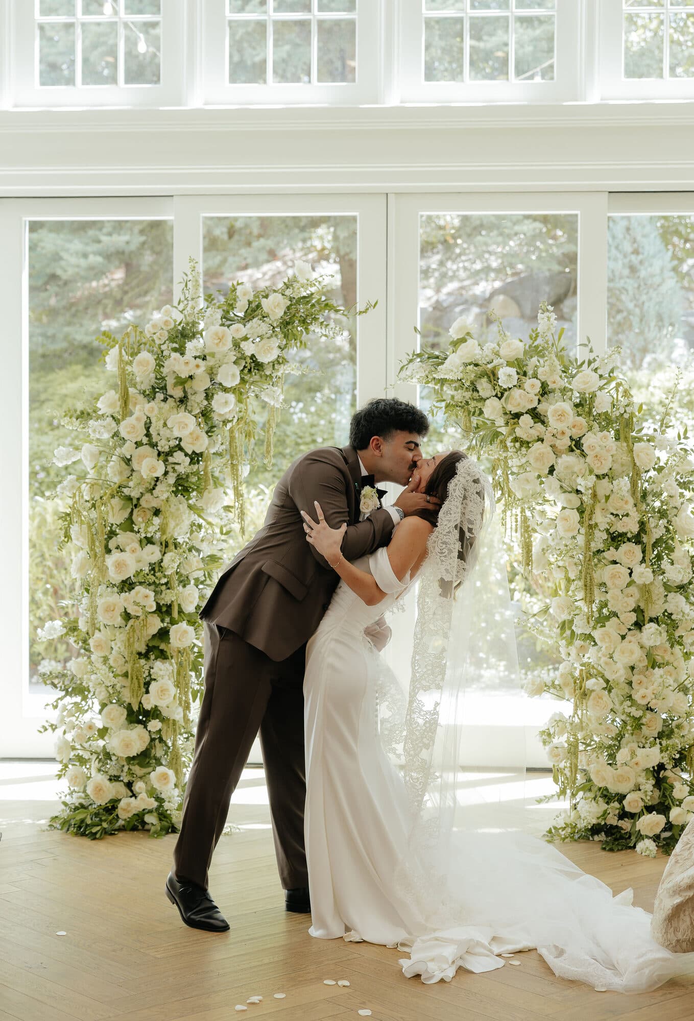 Bride and groom kissing beneath a floral ceremony arch