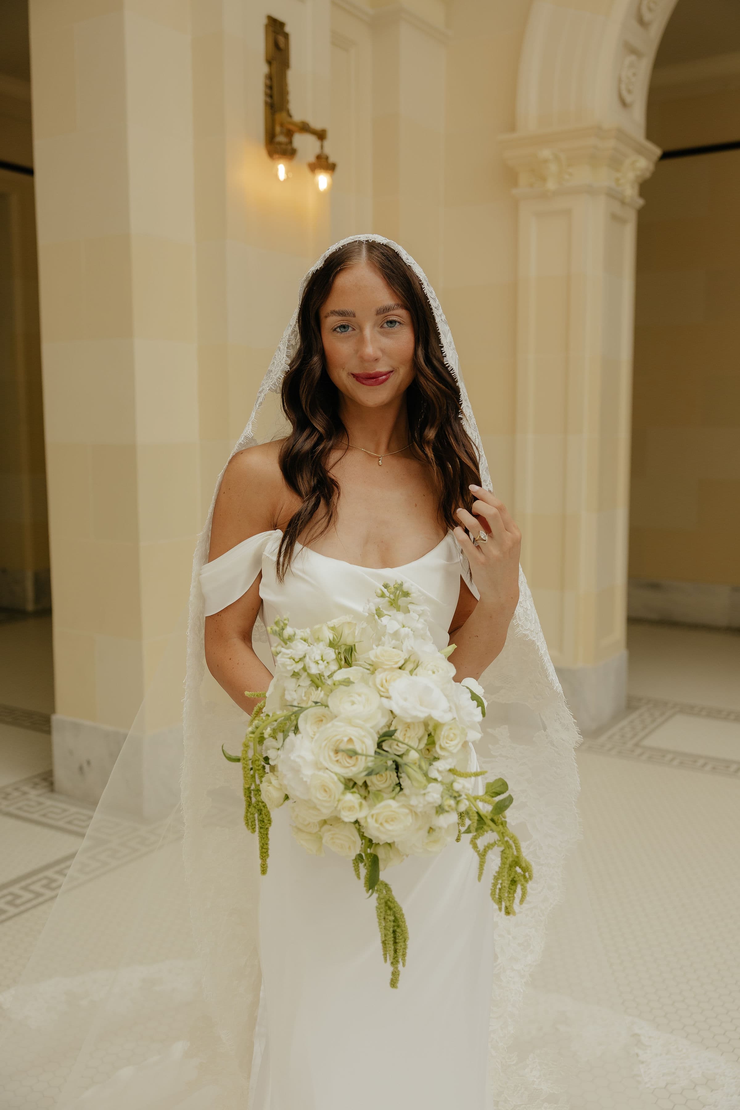 Bride in a lace veil holding a white rose bouquet