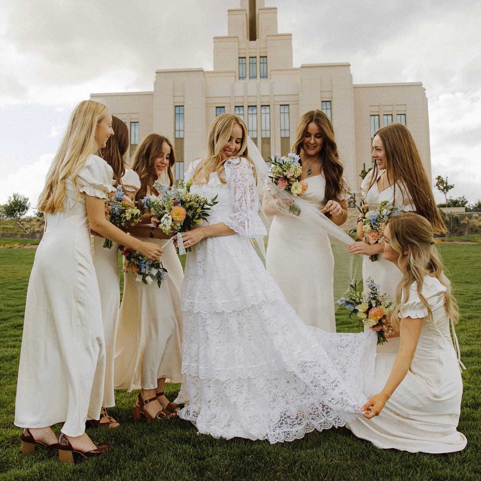 Bride and her bridesmaids holding pastel wildflower bouquets on the lawn outside a temple