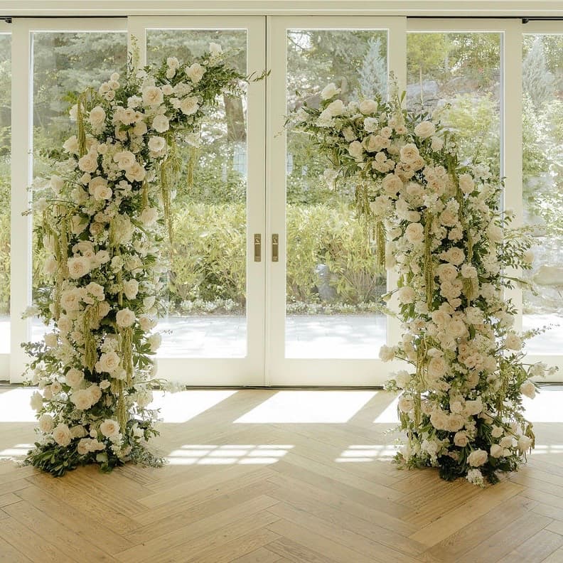 Pair of white rose and greenery ceremony columns framing glass double doors