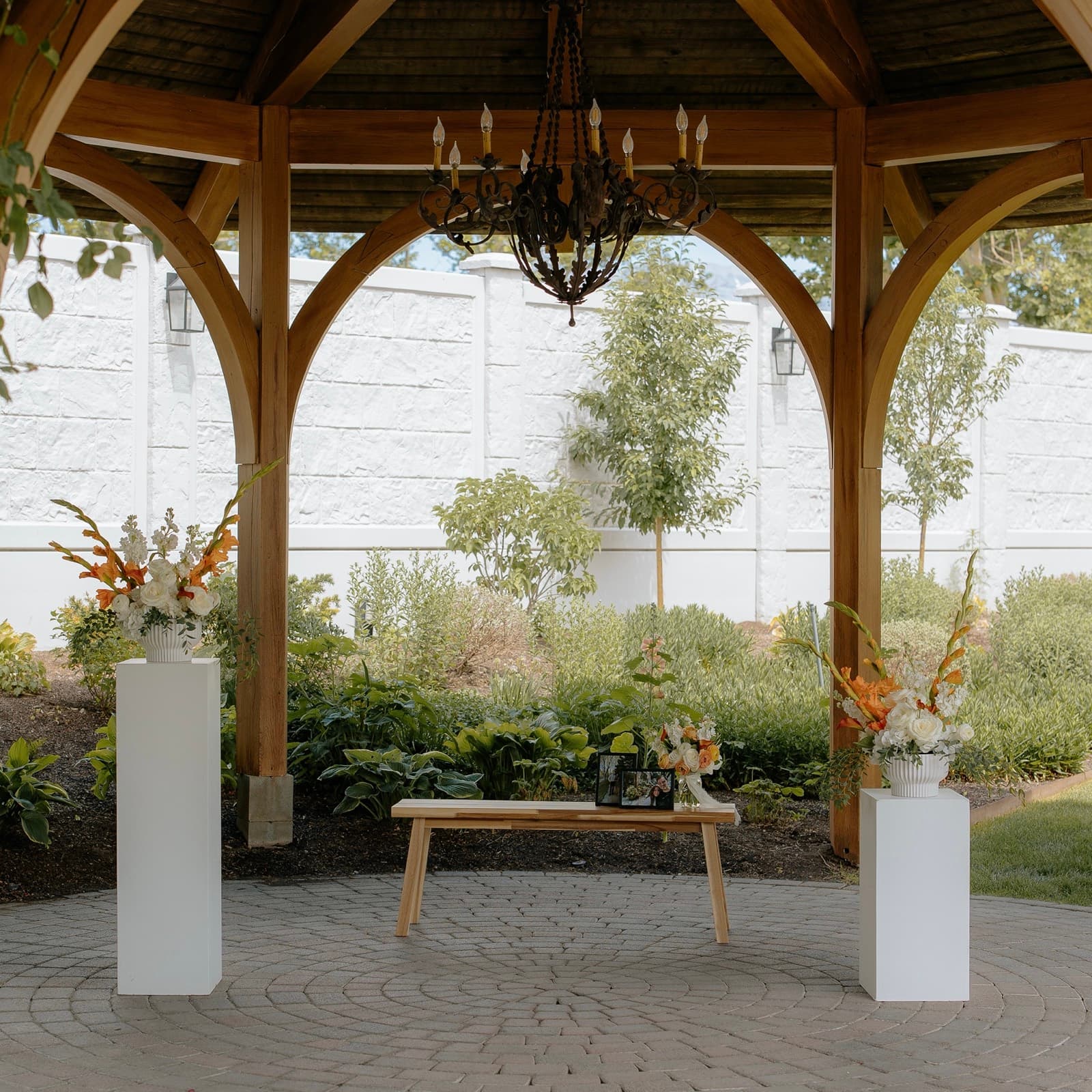 White pedestals with peach and cream arrangements flanking a welcome table inside a wooden gazebo