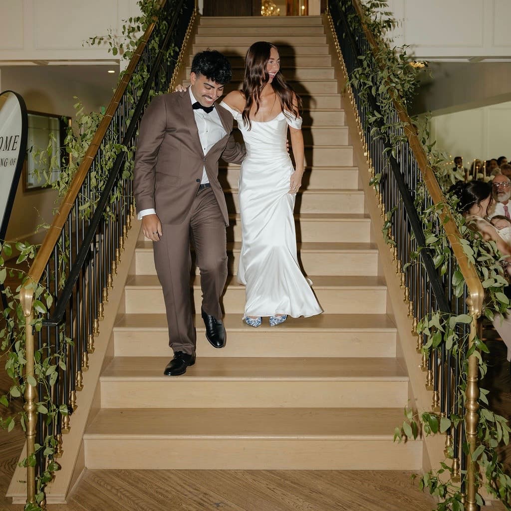 Newlyweds walking down a staircase lined with trailing greenery garlands